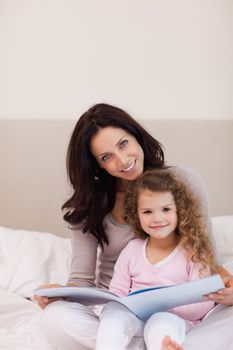 Young mother and daughter reading a book together on the bed