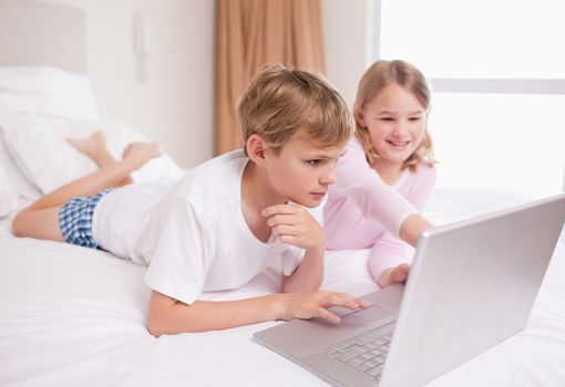 Siblings using a notebook in a bedroom