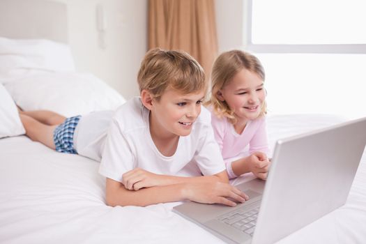 Smiling children using a notebook in a bedroom