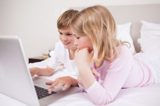 Smiling children using a laptop in a bedroom