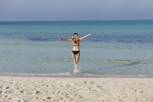 Young woman with black bikini girl on the beach in the sea jumping in the summer holidays