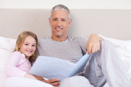 Smiling father reading a story to his daughter in a bedroom