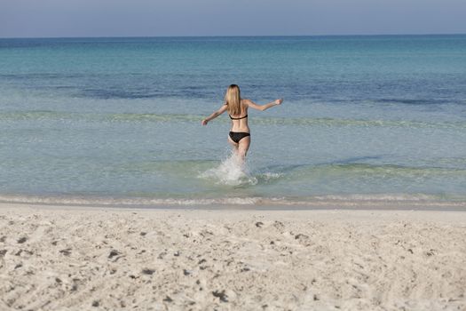 Young woman with black bikini girl on the beach in the sea jumping in the summer holidays