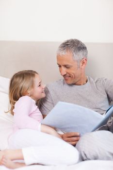 Portrait of a smiling father reading a story to his daughter in a bedroom