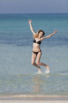 Girl young woman jumping in the water at the beach jumping happily in the sea in summer vacation