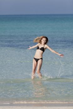 Girl young woman jumping in the water at the beach jumping happily in the sea in summer vacation