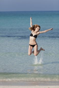 Girl young woman jumping in the water at the beach jumping happily in the sea in summer vacation