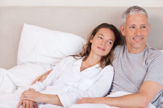 Happy couple lying on a bed looking away from the camera
