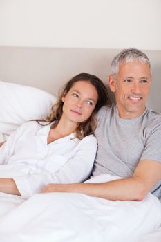 Portrait of a happy couple lying on a bed while looking away from the camera