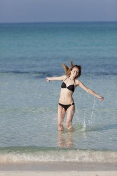 Girl young woman jumping in the water at the beach jumping happily in the sea in summer vacation