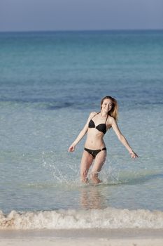 Girl young woman jumping in the water at the beach jumping happily in the sea in summer vacation