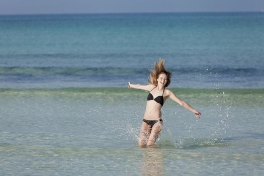 Girl, young woman jumping in the water at the beach jumping happily in the sea in summer vacation