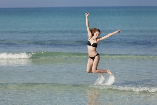 Girl, young woman jumping in the water at the beach jumping happily in the sea in summer vacation