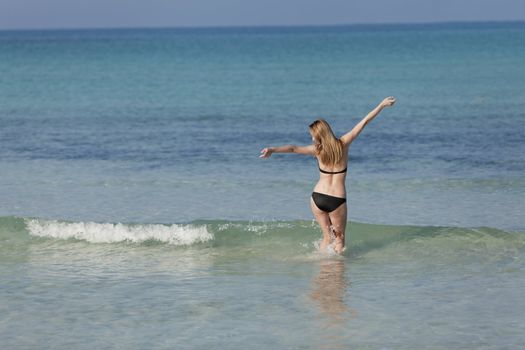 Young woman with black bikini girl on the beach in the sea jumping in the summer holidays