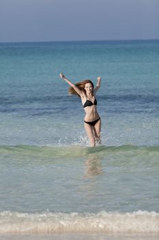 Young woman with black bikini girl on the beach in the sea jumping in the summer holidays