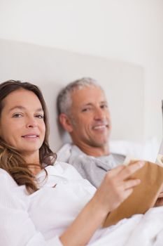Portrait of a woman reading a book while her husband is reading the news in their bedroom