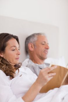 Portrait of a woman reading a book while her husband is reading a newspaper in their bedroom
