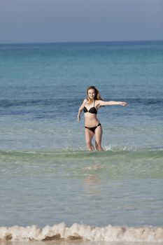 Young woman with black bikini girl on the beach in the sea jumping in the summer holidays