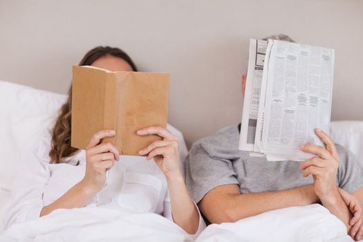 Woman reading a book while her companion is reading a newspaper in their bedroom
