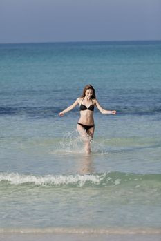 Young woman with black bikini girl on the beach in the sea jumping in the summer holidays