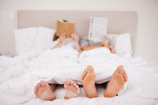 Couple reading while hiding their faces in their bedroom