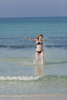 Young woman with black bikini girl on the beach in the sea jumping in the summer holidays