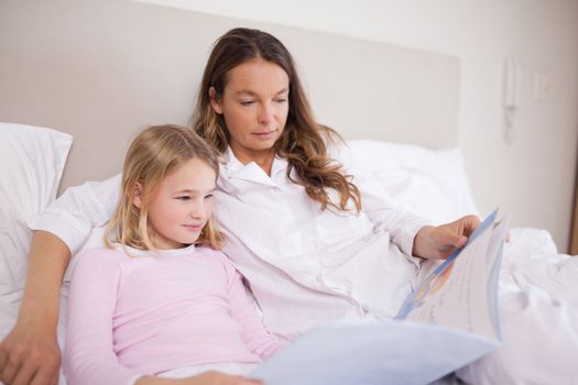 Girl reading a book with her mother in a bedroom
