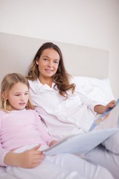 Portrait of a girl reading a book with her mother in a bedroom