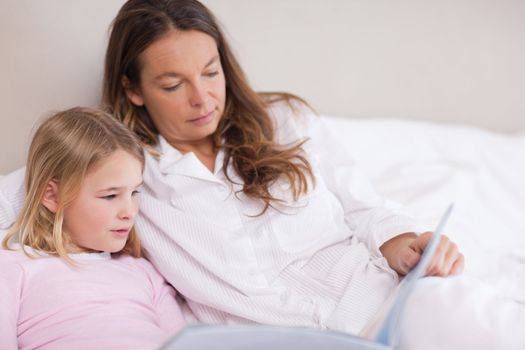 Little girl reading a book with her mother in a bedroom