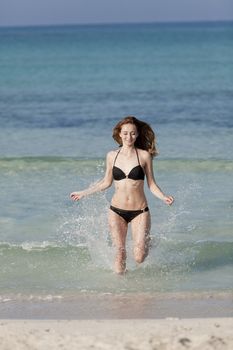 Young woman with black bikini girl on the beach in the sea jumping in the summer holidays