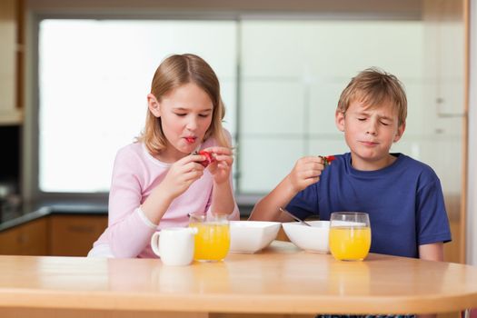 Siblings eating strawberries for breakfast in a kitchen