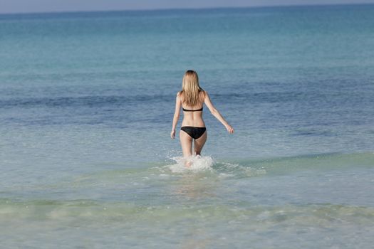 Young woman with black bikini girl on the beach in the sea jumping in the summer holidays