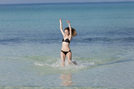 Young woman with black bikini girl on the beach in the sea jumping in the summer holidays
