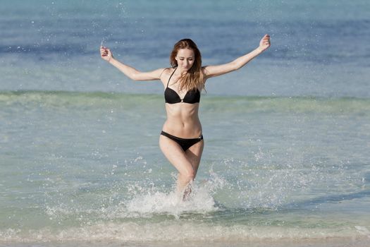 Young woman with black bikini girl on the beach in the sea jumping in the summer holidays