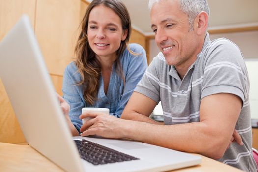 Couple using a laptop while having coffee in their kitchen