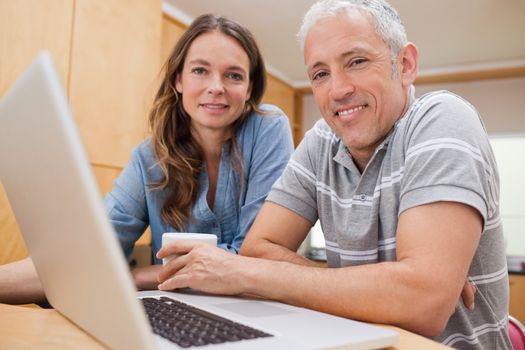 Couple using a laptop while having tea in their kitchen