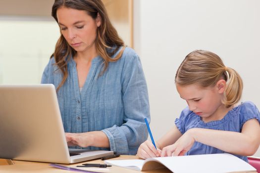 Girl doing her homework while her mother is using laptop in a kitchen