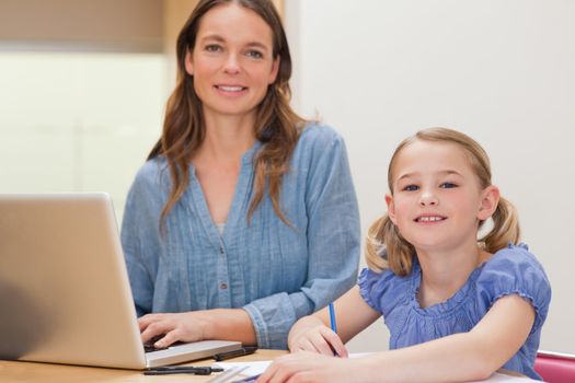 Girl doing her homework while her mother is using notebook in a kitchen