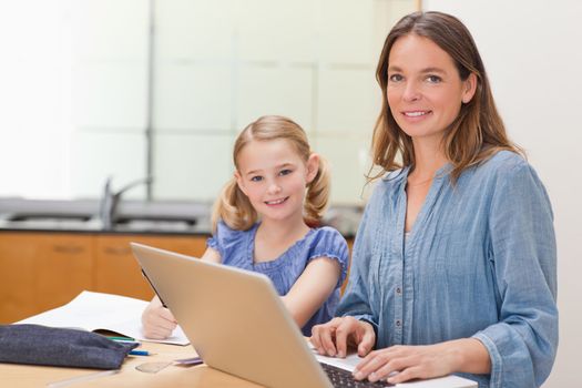 Girl doing her homework while her mother is working with laptop in a kitchen