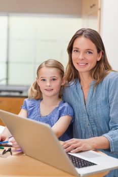 Portrait of a girl doing her homework while her mother is working with laptop in a kitchen