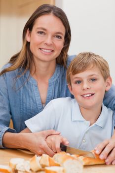 Portrait of a mother slicing bread with her son in a kitchen