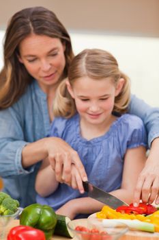 Portrait of a mother slicing pepper with her daughter in a kitchen