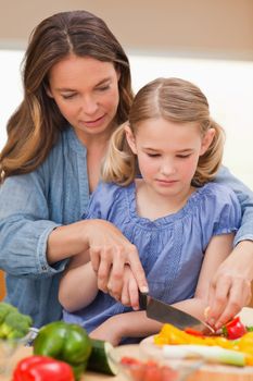 Portrait of a woman slicing pepper with her daughter in a kitchen