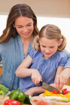 Portrait of a mother slicing bell pepper with her daughter in a kitchen