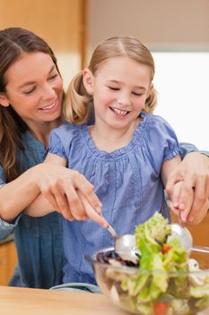 Portrait of a mother preparing a salad with her daughter in a kitchen