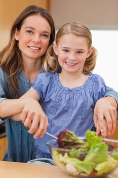 Portrait of a happy mother preparing a salad with her daughter in akitchen