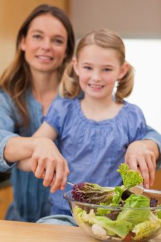Portrait of a happy woman preparing a salad with her daughter in a kitchen