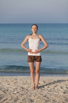 Young sporty woman doing sport yoga on the beach in the sand on the beach in the sun