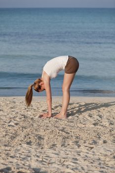 Young sporty woman doing sport yoga on the beach in the sand on the beach in the sun