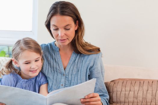 Mother reading a book to her daughter in a living room